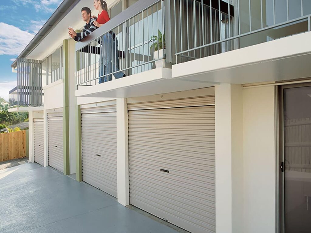 Two people standing on a balcony of a unit above 2 garage doors
